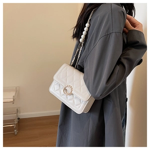 Close-up of white quilted crossbody bag with gold pearl buckle and chain strap on model