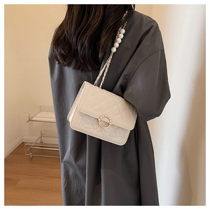 Detail of cream quilted crossbody bag with pearl ring buckle and chain strap on model