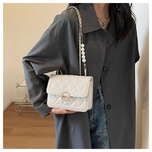 Detail of white quilted crossbody bag featuring a pearl ring clasp and pearl chain strap