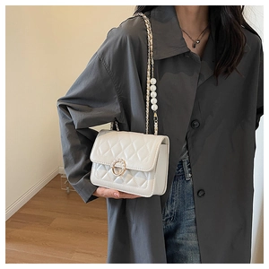 Detailed view of white quilted shoulder bag with elegant pearl clasp and strap on model
