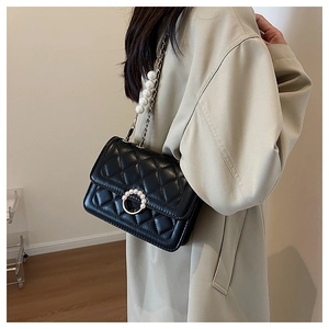 Detail of black quilted leather shoulder bag with faux pearl chain and gold circular clasp