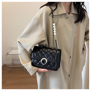 Detail of black quilted shoulder bag featuring round pearl buckle and ornate pearl chain strap