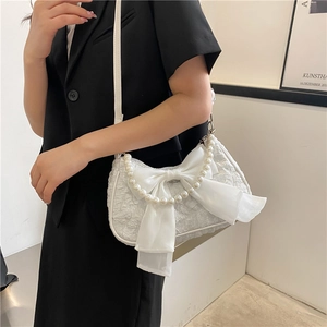 Borsa bianca con manico di perle e grande fiocco indossata su un completo nero