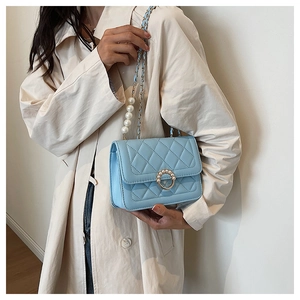 Detail of light blue quilted crossbody bag with pearl strap and decorative buckle clasp