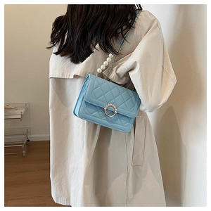 Detail of light blue quilted mini bag with pearl chain and gold lock worn over beige coat