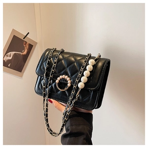 Detail of black quilted leather handbag featuring a large pearl handle and gold chain strap