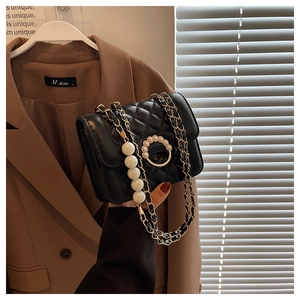Close-up of black quilted mini bag with pearl circle lock and elegant gold chain strap