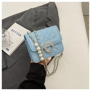 Detail of light blue quilted mini bag with pearl-inlaid gold buckle and pearl chain strap