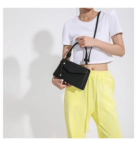 Detail of black structured flap bag featuring a unique knotted handle and gold hardware