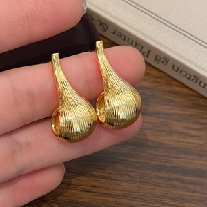 Detail of gold teardrop earrings with brushed metal texture held in hand near a book