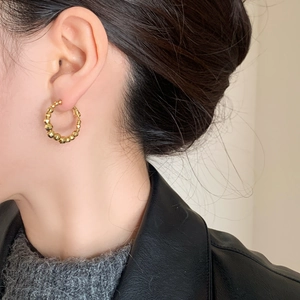 Close-up of a faceted gold-plated bead hoop earring worn by a model in trendy style