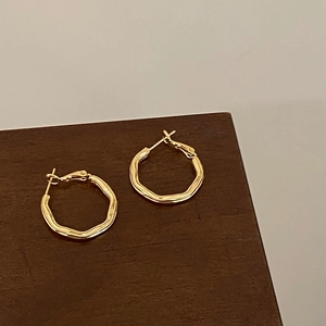 Close-up of wavy gold plated hoop earrings with textured finish on a dark wooden surface