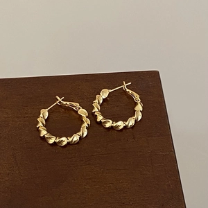 Detail of gold-plated twisted hoop earrings with unique metallic ripple texture on wood