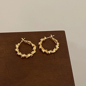 Detail of gold hoop earrings with twisted leaf texture on a wooden pedestal base
