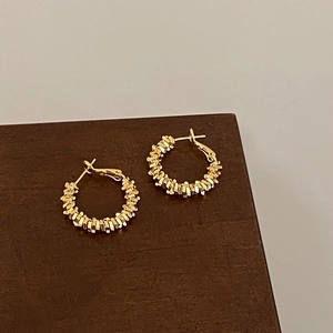 Detail of gold-plated hoop earrings with unique layered texture on wooden display
