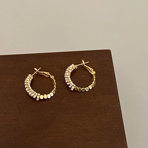 Detail of gold-plated hoop earrings with sparkling rhinestones and metal disc textures
