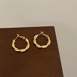 Detail of twisted gold-plated hoop earrings with a textured weave design on a wood stand