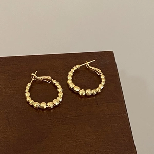 Detail of faceted gold-plated beads on hoop earrings over a wooden surface