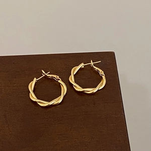 Detail of twisted gold-plated hoop earrings with a textured knot design and polished finish
