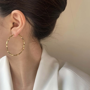 Chic geometric spiral twisted gold plated hoop earrings worn by a model in white
