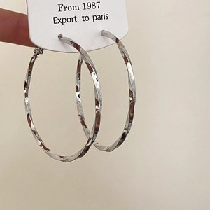 Close-up of large twisted silver hoop earrings with a textured hammered metal finish