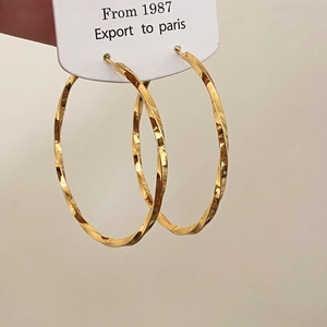 Macro shot of large twisted geometric hoop earrings with polished gold-plated texture