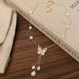 Detail of butterfly necklace with gold tassels and freshwater pearls on rustic background