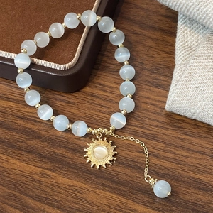Bracelet en perles d'œil de chat naturel avec pendentif soleil doré sur fond texturé