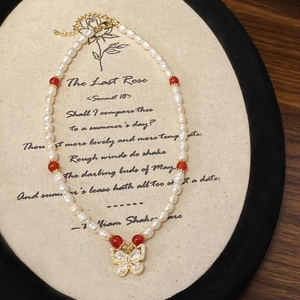 Détail du collier de perles avec pendentif papillon doré et perles rouges sur fond vintage