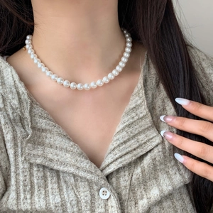 Elegant white pearl necklace with gold clasp worn by a model in casual attire