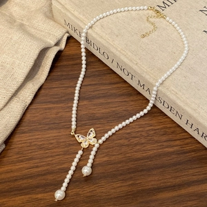 Detail of a pearl necklace with a gold butterfly pendant on a dark wooden surface
