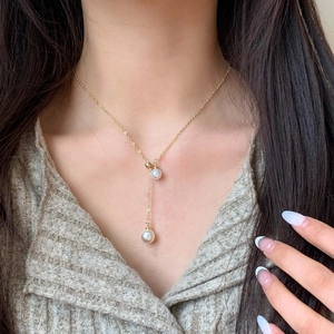 Elegant gold Y-shaped necklace with white pearl pendants worn on a female model