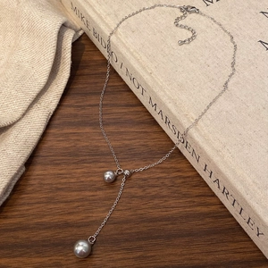 Detail of silver Y-shaped pearl necklace with grey beads on a rustic book cover