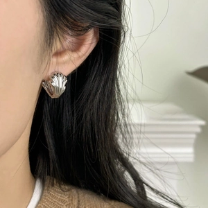 Detailed view of a silver shell-shaped earring on ear with polished metallic texture