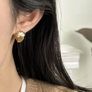 Close-up of model wearing golden shell earrings with detailed vertical wave texture