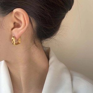 Elegant gold square quilted earrings with black texture lines on a female model