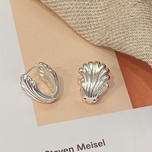 Detailed view of silver shell-textured earrings with 18K gold plating on a warm backdrop