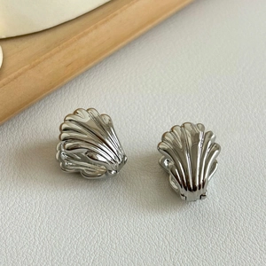 Macro shot of silver shell-textured stud earrings on a white leather background