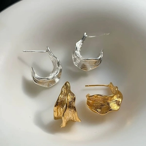 Nahaufnahme von gold- und silbernen C-Ohrringen mit unregelmäßigen Falten