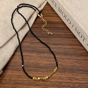 Detail of black faceted bead necklace with gold square accents on wood background
