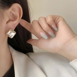 Detail of square vintage earring with gold border and pearl-like center on model