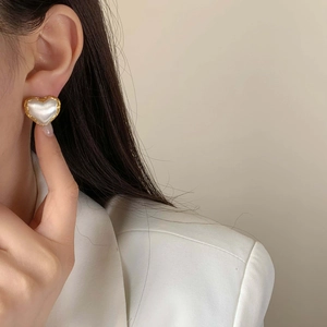 Elegant gold wavy heart earrings with white pearlescent stone inlay on a model