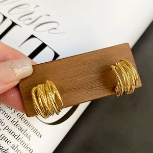 Close-up of golden multi-layered wire wrapped C-shaped earrings held on wooden tray