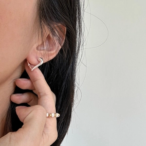 Detail showing heart-shaped hoop earrings and a pearl beaded ring on a female model