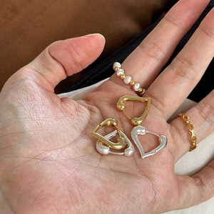 Detailed close-up of heart-shaped gold earrings and minimalist pearl beaded rings on palm