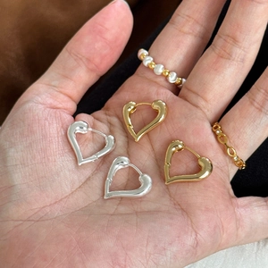 Handheld view of gold and silver heart-shaped hoop earrings with smooth metallic finish