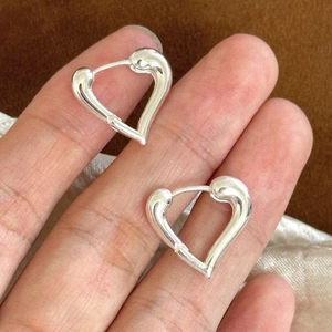 Detail view of heart-shaped silver earrings held by hand on soft plush surface