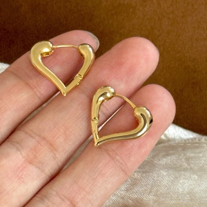 Detailed view of gold heart earrings held in hand to show size and polished finish