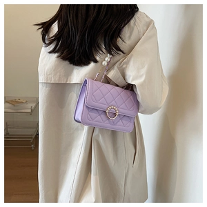 Detail of purple quilted shoulder bag with pearl accents on a beige coat outfit