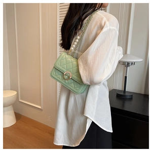 Close-up of light green quilted crossbody bag featuring a pearl-embellished round clasp